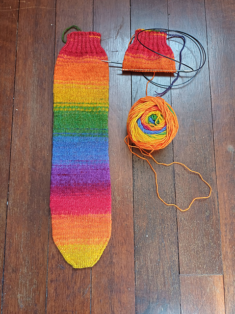 One complete knitted sock in rainbow colours, one partly knitted sock, a ball of rainbow yarn