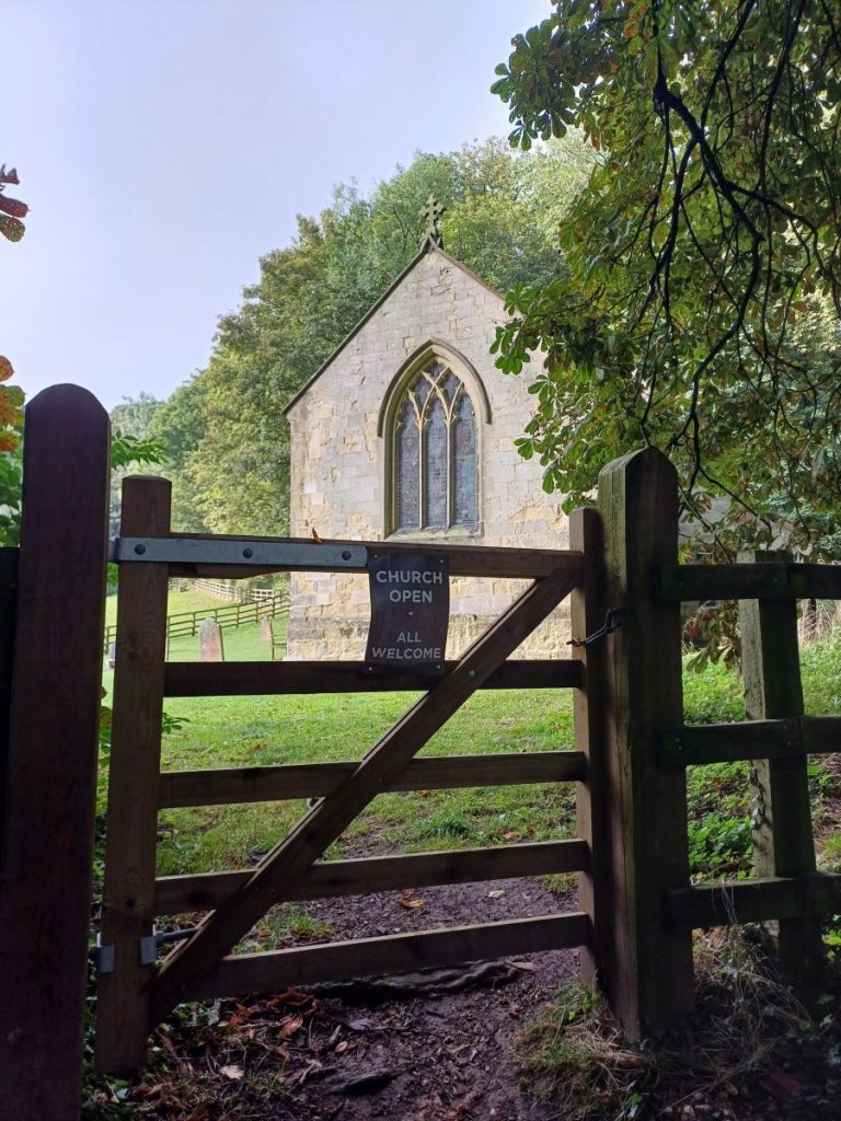 Picture shows a wooden gate in the foreground. In the background is a small country church.