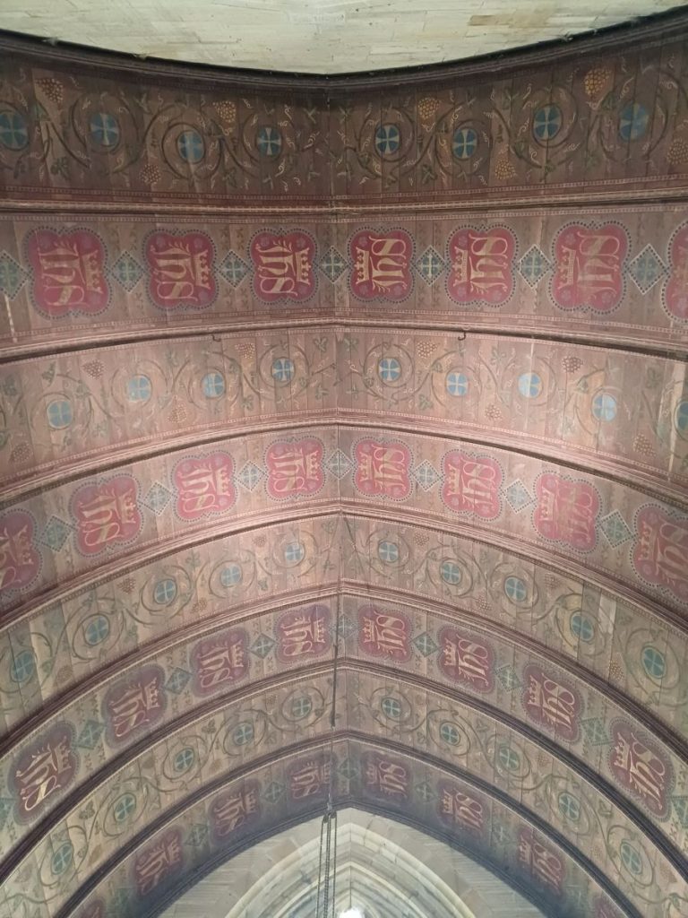 Picture shows the underside of a church roof, lavishly decorated mainly in red tones.