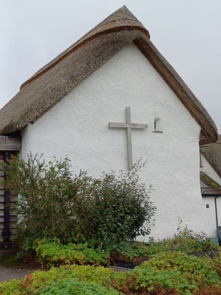 Picture shows a whitewashed building with a thatched roof. A large cross is on the end of the building.