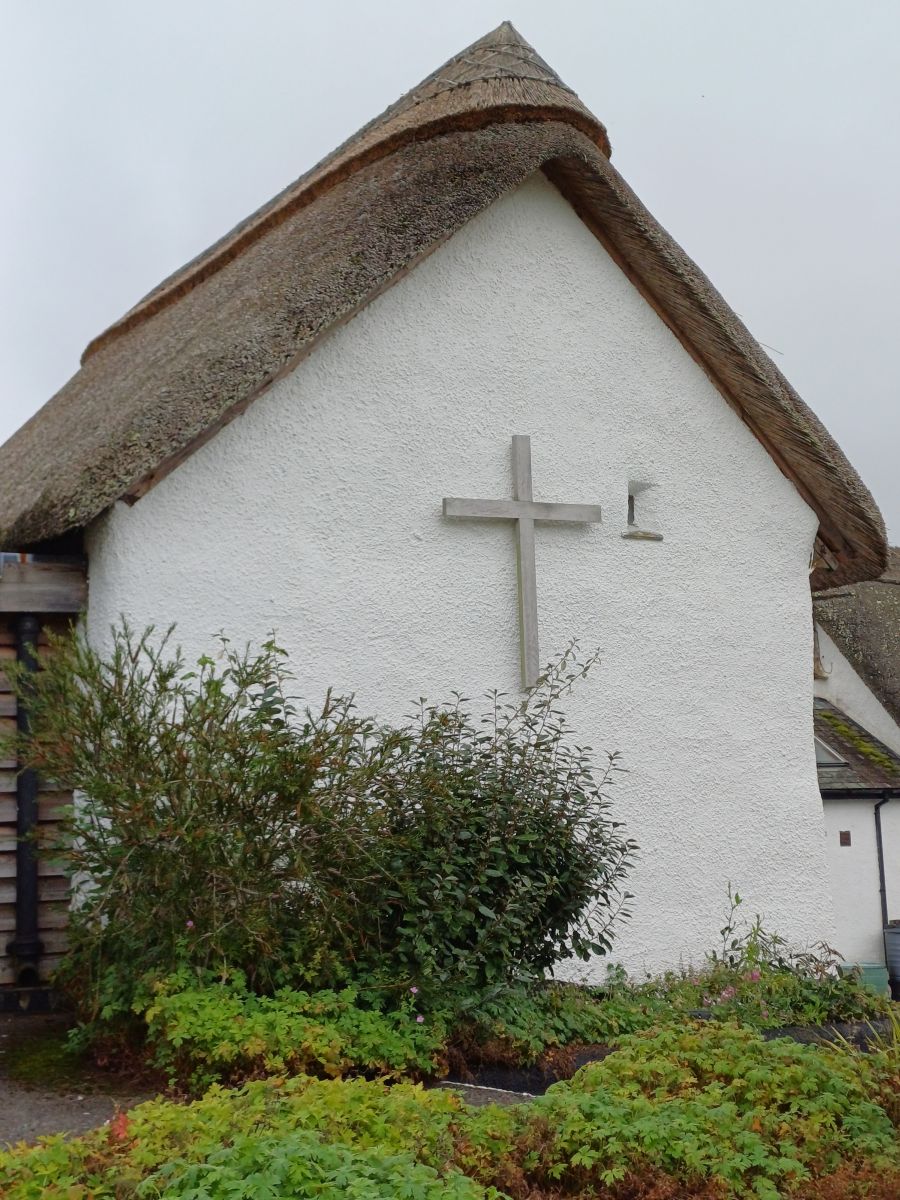 Picture shows a whitewashed building with a thatched roof. A large cross is on the end of the building.