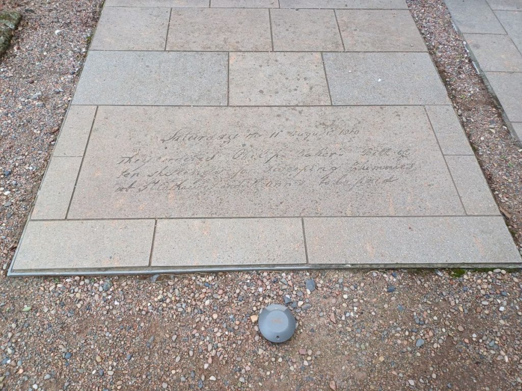 Picture shows a series of stone slabs set into the ground, on one of which is carved, in a facsimile of handwriting of the time "Saturday 11th August 1810 - They ordered Philip Baker's Bill of ten shillings for sweeping chimneys of St Catherines and St Ann to be paid"